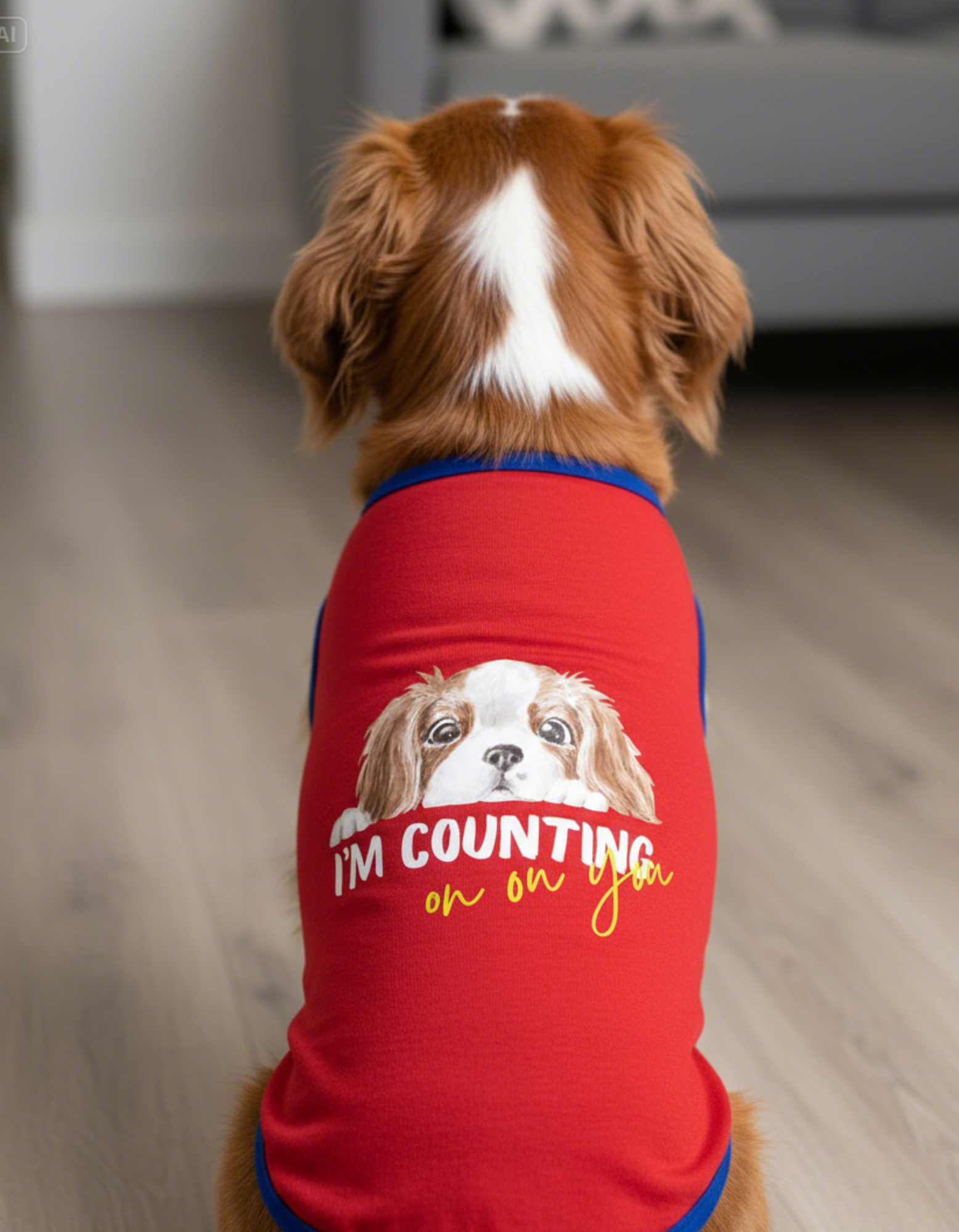 Dog wearing a red shirt with a graphic of another dog and text on a wooden floor.