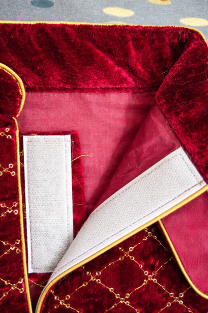 Close-up of a red velvet fabric with gold trim and white lining.